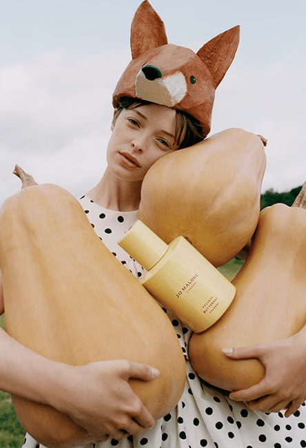Modelo con gorro de zorro sosteniendo calabazas y una botella de perfume Jo Malone London